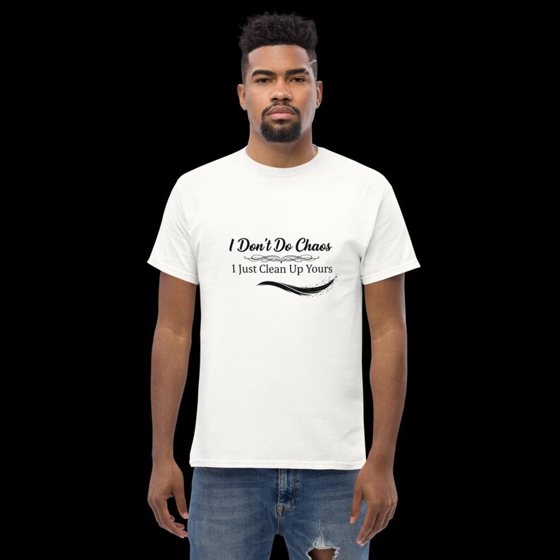 Puede incluir: Una camiseta blanca de manga corta con el texto impreso en negro I Don't Do Chaos I Just Clean Up Yours, que incluye un adorno decorativo y una l&iacute;nea curva bajo las letras, combinada con vaqueros azules sobre un fondo negro.