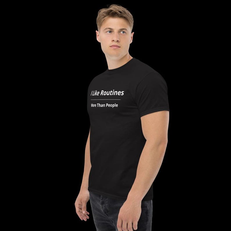K&ouml;nnte beinhalten: Ein schwarzes kurz&auml;rmeliges T-Shirt mit wei&szlig;em Text auf der Brust, der I Like Routines lautet, gefolgt von einer horizontalen Linie und dem Text More Than People. Das T-Shirt hat einen Rundhalsausschnitt und wird zu einer dunkelgrauen Jeans getragen.
