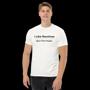 May include: A white short-sleeved t-shirt featuring the black text "I Like Routines" on the top line, a horizontal black line underneath, and the text "More Than People" on the bottom line, centred on the chest area of the garment.