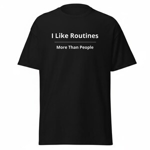 K&ouml;nnte beinhalten: Ein schwarzes kurz&auml;rmeliges T-Shirt mit wei&szlig;em Text auf der Brust, der I Like Routines lautet, mit einer horizontalen Linie darunter und dem Text More Than People unter der Linie. Das T-Shirt hat einen Rundhalsausschnitt und eine Standardpassform.