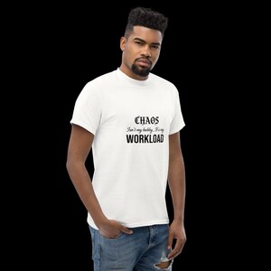 May include: A white short-sleeved t-shirt featuring black text on the chest that reads "CHAOS Isn't my hobby, It's my WORKLOAD" in a combination of gothic and sans-serif fonts. The shirt is paired with blue denim jeans.