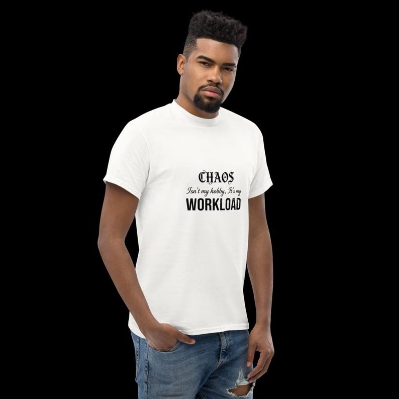 May include: A white short-sleeved t-shirt featuring black text on the chest that reads "CHAOS Isn't my hobby, It's my WORKLOAD" in a combination of gothic and sans-serif fonts. The shirt is paired with blue denim jeans.