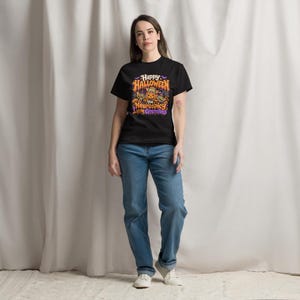 May include: A black short-sleeved t-shirt featuring a colorful Halloween-themed graphic print. The design includes a central pumpkin, bats, and the text "Happy Halloween you Neurospicy little Gremlins" in orange, purple, and white lettering.