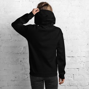 K&ouml;nnte beinhalten: Ein einfarbiger, schwarzer Kapuzenpullover mit langen &Auml;rmeln, einer gro&szlig;en Kapuze, gerippten &Auml;rmelb&uuml;ndchen und einem geraden Saum. Das Kleidungsst&uuml;ck ist von hinten zu sehen und zeigt eine schlichte, ungemusterte schwarze Stoffkonstruktion.