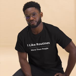 K&ouml;nnte beinhalten: Ein schwarzes Kurzarm-T-Shirt mit dem wei&szlig;en Text "I Like Routines" &uuml;ber einer horizontalen Linie und dem darunter gedruckten Text "More Than People". Das T-Shirt hat einen Rundhalsausschnitt und eine Standardpassform aus einfarbigem Stoff.