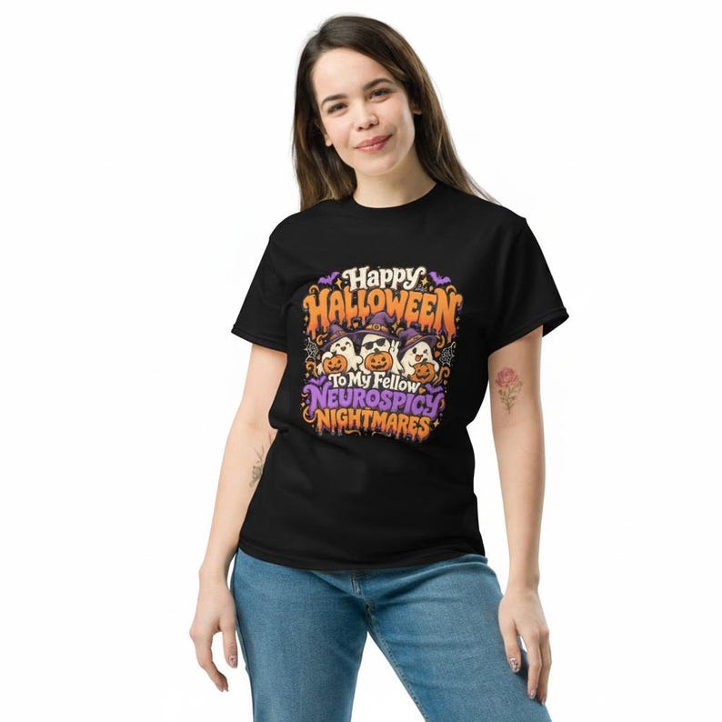 May include: A black short-sleeved t-shirt featuring a colourful graphic print with three ghosts wearing witch hats and holding pumpkins. The text reads Happy Halloween To My Fellow Neurospicy Nightmares in orange and purple stylised lettering.