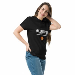 May include: A black short-sleeved t-shirt featuring the white text (NEURO)SPICY and Pumpkin Latte For Me Please, accompanied by a small orange jack-o'-lantern graphic centered on the chest area, paired with blue denim jeans.