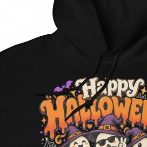 May include: A black hooded sweatshirt featuring a graphic print with the text Happy Halloween in orange and white lettering. The design includes three white ghost characters wearing purple witch hats, with one ghost wearing black sunglasses.