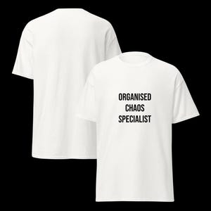 May include: A white short-sleeved t-shirt featuring the black text "ORGANISED CHAOS SPECIALIST" printed on the front chest area. The garment has a crew neckline and a standard fit, shown from both the front and back views against a black background.