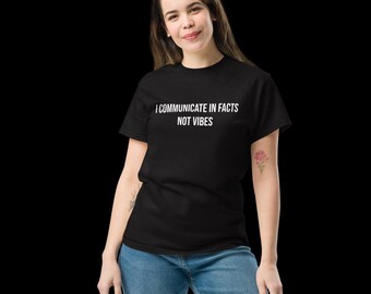 May include: A black short-sleeved t-shirt featuring the white text "I COMMUNICATE IN FACTS NOT VIBES" printed across the chest. The garment is paired with blue denim jeans, creating a casual look with a clear, bold statement in white lettering.