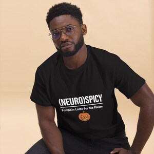May include: A black short-sleeved t-shirt featuring white text that reads (NEURO)SPICY and Pumpkin Latte For Me Please, accompanied by a small orange jack-o'-lantern graphic centered below the text on the front of the garment.