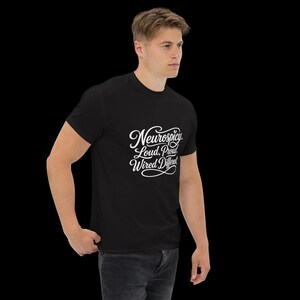 K&ouml;nnte beinhalten: Ein schwarzes Kurzarm-T-Shirt mit wei&szlig;em Schreibschrift-Text auf der Brust, der Neurospicy. Loud, Proud, Wired Different lautet. Das T-Shirt hat einen Rundhalsausschnitt und eine Standardpassform vor einem schlichten schwarzen Hintergrund.