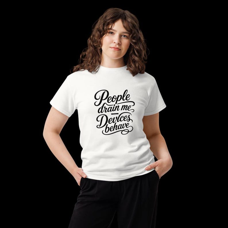Op de afbeelding: Een wit t-shirt met korte mouwen en zwarte cursieve tekst op de borst met de tekst People drain me, Devices behave. Het shirt heeft een ronde hals en een standaard pasvorm, gepresenteerd tegen een effen zwarte achtergrond voor goede zichtbaarheid.