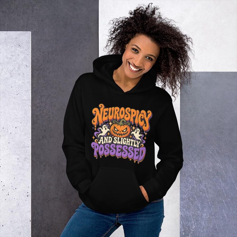 May include: A black hooded sweatshirt featuring a graphic print with an orange jack-o'-lantern, two white ghosts, and the text "NEUROSPICY AND SLIGHTLY POSSESSED" in orange and purple lettering with a dripping effect.