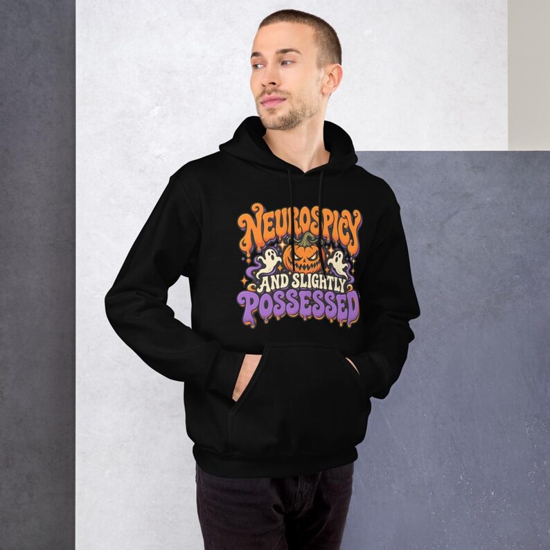 May include: A black hooded sweatshirt featuring a graphic print with the text "NEUROSPICY AND SLIGHTLY POSSESSED" in orange and purple. The design includes a central jack-o'-lantern, two white ghosts, and small yellow stars on the front.