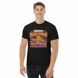 May include: A black short-sleeve t-shirt featuring a colorful graphic print with the text "Happy Halloween You Neurospicy Little Gremlins". The design includes three green creatures, a carved jack-o'-lantern, bats, and stars in orange and purple.