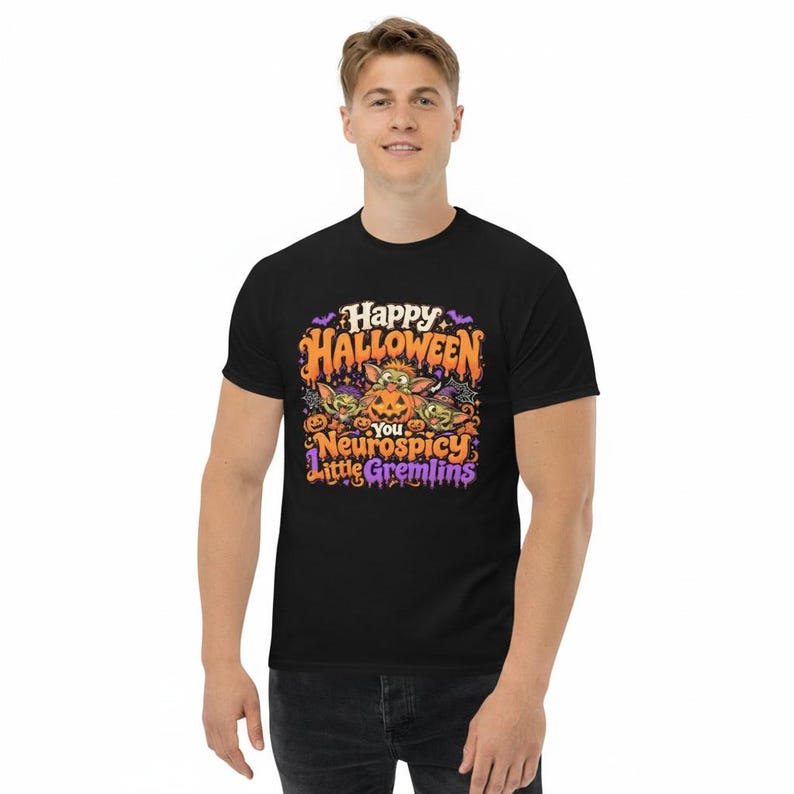 May include: A black short-sleeve t-shirt featuring a colorful graphic print with the text "Happy Halloween You Neurospicy Little Gremlins". The design includes three green creatures, a carved jack-o'-lantern, bats, and stars in orange and purple.