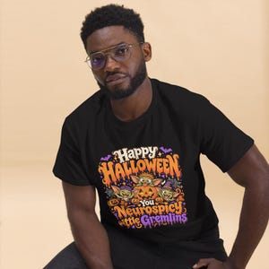 May include: A black short-sleeved t-shirt featuring a colorful graphic with the text Happy Halloween You Neurospicy little Gremlins. The design includes three green creatures, orange pumpkins, purple bats, and spiderwebs in a vibrant cartoon style.