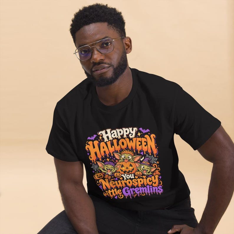 May include: A black short-sleeved t-shirt featuring a colorful graphic with the text Happy Halloween You Neurospicy little Gremlins. The design includes three green creatures, orange pumpkins, purple bats, and spiderwebs in a vibrant cartoon style.