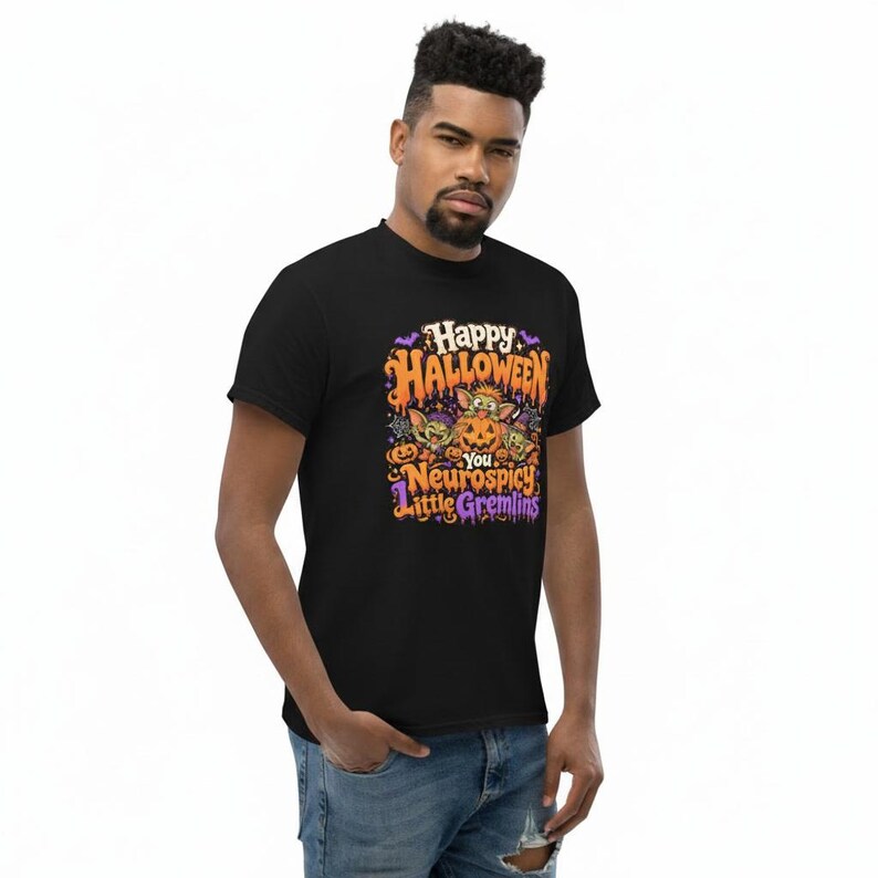 May include: A black short-sleeved t-shirt featuring a colorful graphic print with the text "Happy Halloween You Neurospicy Little Gremlins". The design includes illustrations of three small creatures, a carved pumpkin, bats, and spiderwebs.