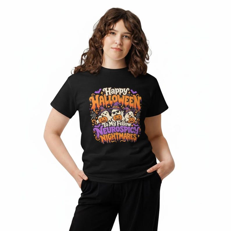May include: A black short-sleeved t-shirt featuring a colourful graphic with three ghosts wearing purple witch hats and holding orange jack-o'-lanterns. The text reads Happy Halloween To My Fellow NEUROSPICY NIGHTMARES in orange and purple.