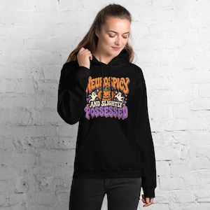 May include: A black hooded sweatshirt featuring a graphic print with an orange pumpkin, two white ghosts, and the text "NEUROSPICY AND SLIGHTLY POSSESSED" in orange and purple lettering on the front chest area.