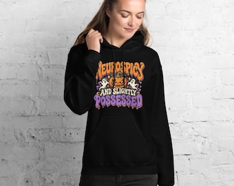 Könnte beinhalten: Ein schwarzer Kapuzenpullover mit einem Grafikdruck, der einen orangefarbenen Kürbis, zwei weiße Geister und den Text "NEUROSPICY AND SLIGHTLY POSSESSED" in orangefarbenen und violetten Buchstaben auf der Brust zeigt.