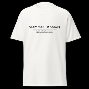 Op de afbeelding: Een wit T-shirt met korte mouwen en zwarte tekst in het midden van de borst met de tekst Scammer TV Shows, met de ondertitel Public Safety for viewers. Free tutorials for criminals, gedrukt in een strak, schreefloos lettertype.