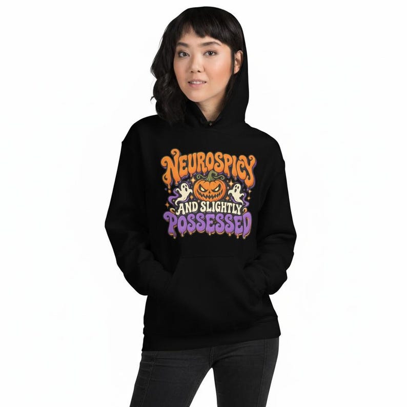 May include: A black hooded sweatshirt featuring a graphic print with an orange jack-o'-lantern, two white ghosts, and the text "NEUROSPICY AND SLIGHTLY POSSESSED" in orange and purple lettering with a dripping effect and small star accents.