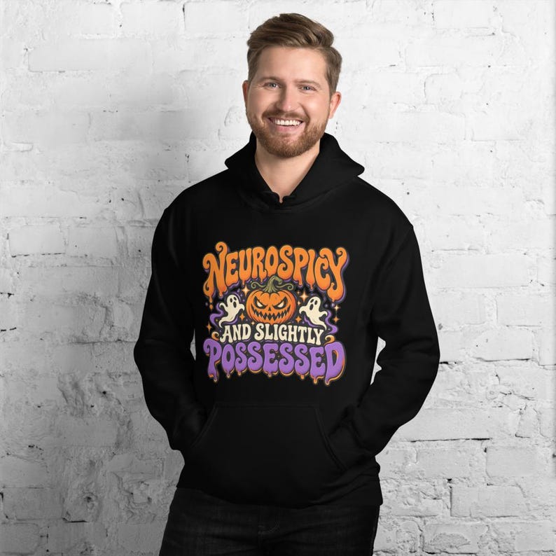 May include: A black hooded sweatshirt featuring a graphic print with an orange jack-o'-lantern, two white ghosts, and purple stars. The text reads "NEUROSPICY AND SLIGHTLY POSSESSED" in a stylized, wavy orange and purple font on the front chest.