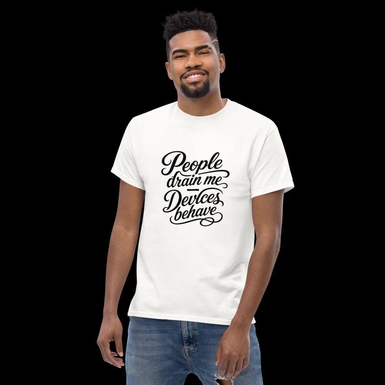 Op de afbeelding: Een wit T-shirt met korte mouwen en zwarte cursieve tekst op de borst met de tekst People drain me, Devices behave. Het shirt heeft een ronde hals en wordt gecombineerd met een blauwe spijkerbroek voor een casual en eenvoudige uitstraling.