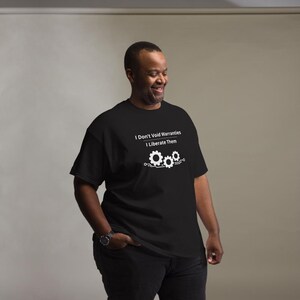 May include: A black short-sleeved t-shirt featuring white text that reads I Don't Void Warranties I Liberate Them above a graphic of three interlocking gears connected by circuit board lines centred on the chest of the garment.