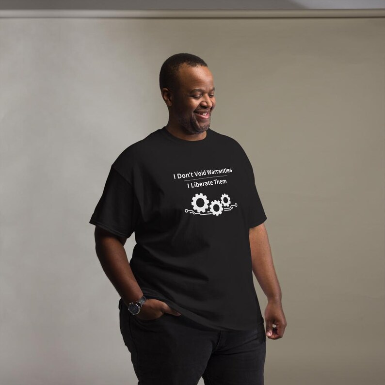 May include: A black short-sleeved t-shirt featuring white text that reads I Don't Void Warranties I Liberate Them above a graphic of three interlocking gears connected by circuit board lines centred on the chest of the garment.
