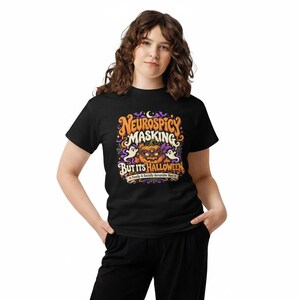 Pu&ograve; includere: Una t-shirt nera con una grafica colorata che riporta il testo "NEUROSPICY MASKING BUT ITS HALLOWEEN" e "Finally A Socially Acceptable Mask". Il disegno include una zucca con una maschera, due fantasmi e dei pipistrelli.