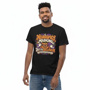 Pu&ograve; includere: Una t-shirt nera a maniche corte con una grafica colorata che riporta il testo "NEUROSPICY MASKING BUT ITS HALLOWEEN" e "Finally A Socially Acceptable Mask". Il disegno include una zucca, due fantasmi e delle stelline.