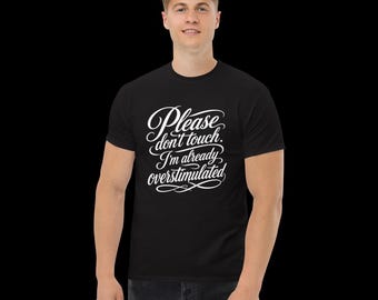 May include: A black short-sleeved t-shirt featuring white cursive text on the chest that reads, Please don't touch. I'm already overstimulated. The garment has a crew neckline and a standard fit, providing a clear view of the printed graphic design.