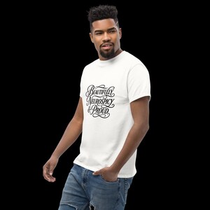 K&ouml;nnte beinhalten: Ein wei&szlig;es Kurzarm-T-Shirt mit schwarzem, kursivem Text auf der Brust, der Beautifully Neurospicy & Proud lautet. Das Shirt hat einen Rundhalsausschnitt und wird mit einer blauen Jeans kombiniert, was ein l&auml;ssiges und klassisches Design ergibt.