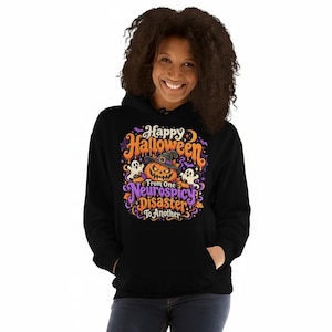 May include: A black hooded sweatshirt featuring a colorful graphic print with a jack-o'-lantern wearing a witch hat, two ghosts, and the text "Happy Halloween From One Neurospicy Disaster To Another" in orange and purple lettering.