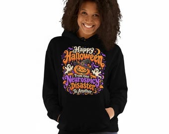 May include: A black hooded sweatshirt featuring a colorful graphic print with a jack-o'-lantern wearing a witch hat, two ghosts, and the text "Happy Halloween From One Neurospicy Disaster To Another" in orange and purple lettering.