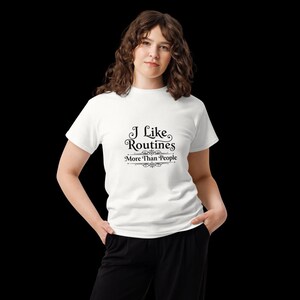 May include: A white short-sleeved t-shirt featuring black text that reads I Like Routines More Than People, centered on the chest. The lettering is styled with decorative flourishes above and below the word Routines and the entire phrase.