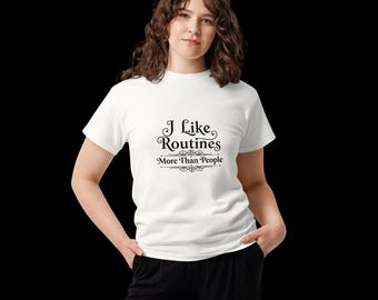 Peut inclure: Un t-shirt blanc à manches courtes avec un texte noir imprimé au centre de la poitrine indiquant I Like Routines More Than People. Le lettrage est orné de fioritures décoratives au-dessus et au-dessous du mot Routines et de la phrase.