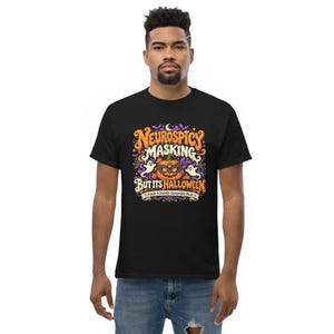 Pu&ograve; includere: Una t-shirt nera con una grafica colorata che riporta il testo "NEUROSPICY MASKING BUT ITS HALLOWEEN" e "Finally A Socially Acceptable Mask". Il disegno include una zucca con una maschera, due fantasmi e alcuni pipistrelli.