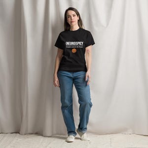 May include: A black short-sleeved t-shirt featuring the white text (NEURO)SPICY and Pumpkin Latte For Me Please, accompanied by a small orange jack-o'-lantern graphic, paired with blue denim jeans and white sneakers.