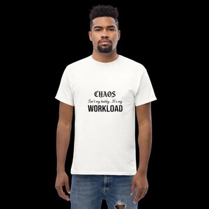 May include: A white short-sleeved t-shirt featuring black text on the chest that reads: CHAOS Isn't my hobby, It's my WORKLOAD. The shirt has a crew neckline and is paired with blue denim jeans that have a distressed detail on the left thigh area.