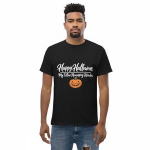 May include: A black short-sleeved t-shirt featuring white cursive text that reads Happy Halloween My Fellow Neurospicy Weirdos above a graphic of an orange jack-o'-lantern with a jagged, menacing grin and triangular eyes centered on the chest.