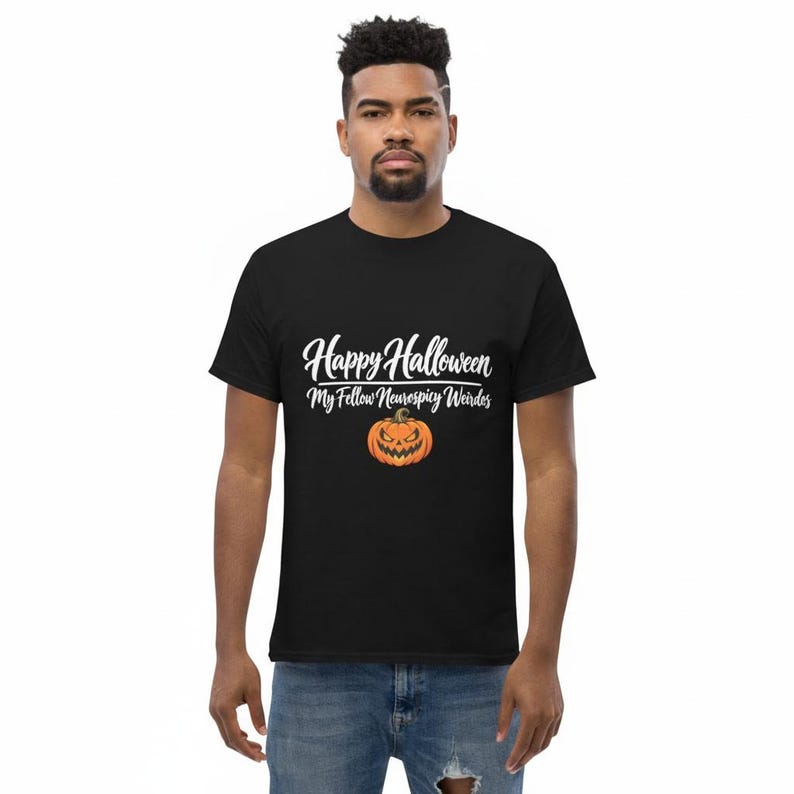May include: A black short-sleeved t-shirt featuring white cursive text that reads Happy Halloween My Fellow Neurospicy Weirdos above a graphic of an orange jack-o'-lantern with a jagged, menacing grin and triangular eyes centered on the chest.