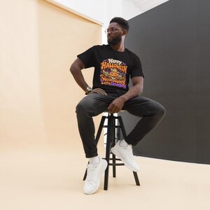 May include: A black short-sleeved t-shirt featuring a colorful Halloween-themed graphic on the chest. The design includes orange and purple text that reads Happy Halloween you Neurospicy Little Gremlins, surrounded by pumpkins and bats.