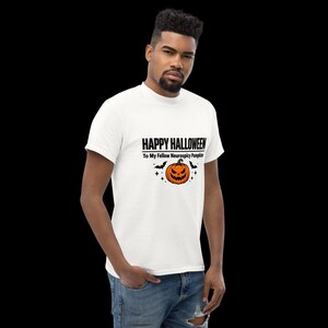 K&ouml;nnte beinhalten: Ein wei&szlig;es Kurzarm-T-Shirt mit einem schwarzen Grafikdruck, der HAPPY HALLOWEEN To My Fellow Neurospicy Pumpkins liest, erg&auml;nzt durch eine orangefarbene K&uuml;rbis-Illustration, kleine schwarze Flederm&auml;use und Sternakzente.