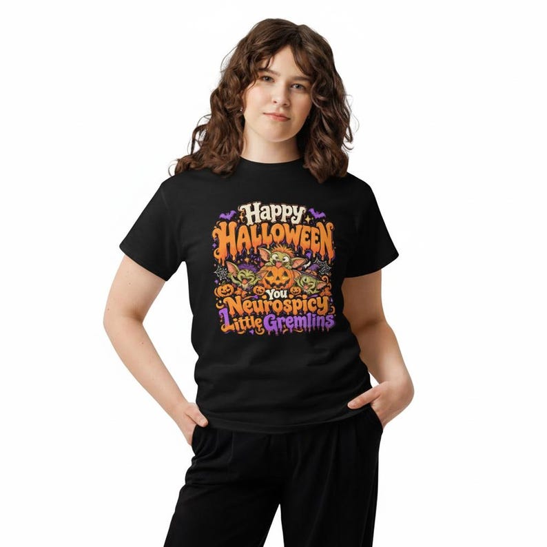 May include: A black short-sleeved t-shirt featuring a colorful Halloween graphic with orange, purple, and green accents. The design includes three small creatures, pumpkins, and the text: Happy Halloween You Neurospicy Little Gremlins.