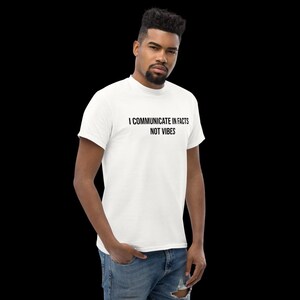Peut inclure: Un t-shirt blanc &agrave; manches courtes avec le texte noir "I COMMUNICATE IN FACTS NOT VIBES" imprim&eacute; sur la poitrine. Le v&ecirc;tement pr&eacute;sente un col rond et une coupe standard, associ&eacute; &agrave; un jean bleu en denim avec un d&eacute;tail us&eacute; au niveau du genou.